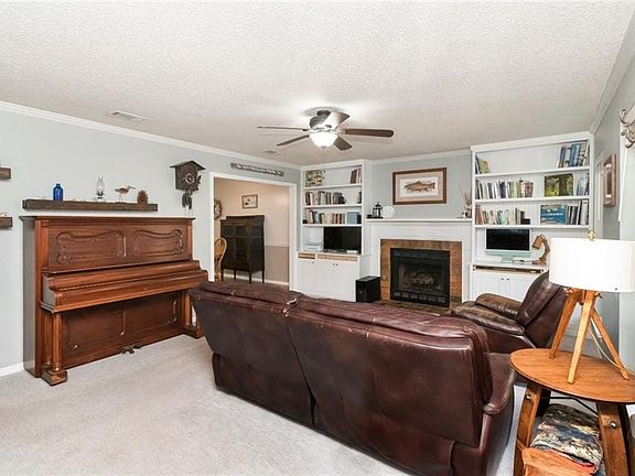 Living room featuring light carpet, a fireplace, a textured ceiling, a ceiling fan, and crown molding