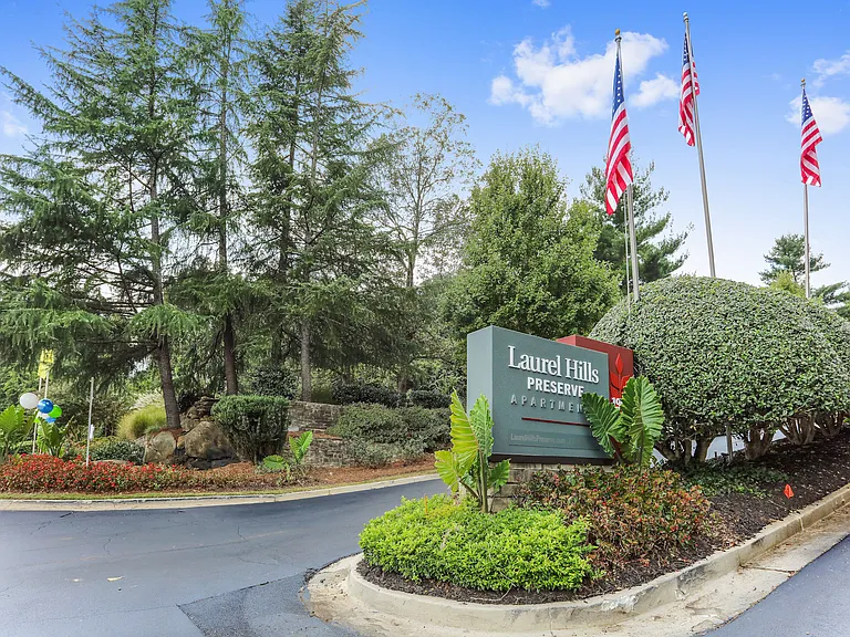 Property sign with lush landscaping of grass, trees, bushes, and flowers.