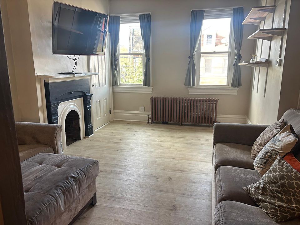 Livingroom featuring (non-functional) fireplace, built in adjustable shelving, windows looking out the front of the house, ceiling fan, and closet. Couches and TV included