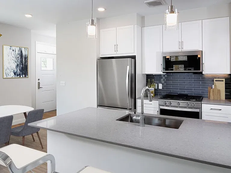 Phase II Renovated Package I apartment kitchen with stainless steel appliances, grey quartz countertops, white cabinetry, dark grey tile backsplash, and hard surface flooring