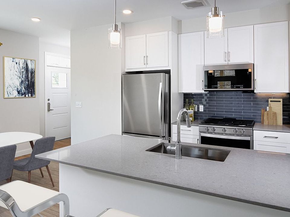 Phase II Renovated Package I apartment kitchen with stainless steel appliances, grey quartz countertops, white cabinetry, dark grey tile backsplash, and hard surface flooring