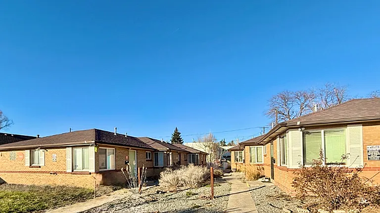 Charming brick duplex units with large windows and a sunny walkway, surrounded by a clear blue sky and peaceful landscaping.