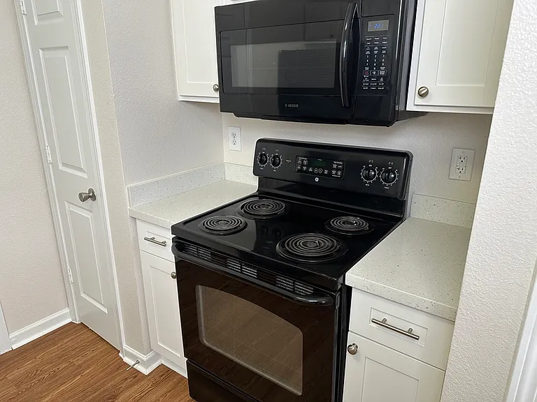 Modern kitchen nook featuring sleek black appliances, pristine white cabinetry, quartz countertops, and stylish wood-style flooring. Modern kitchen nook featuring sleek black appliances, pristine white cabinetry, quartz countertops, and stylish wood-style