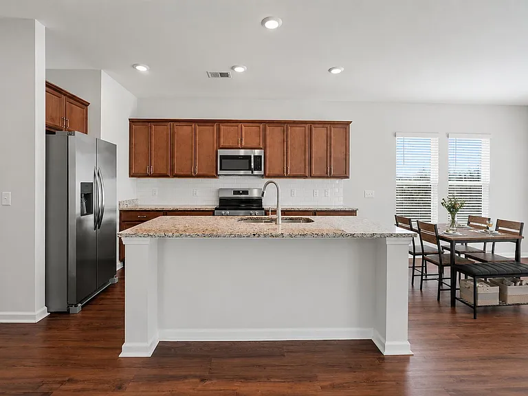 Open kitchen with a large granite island, stainless steel appliances, ample cabinetry, and adjacent dining space by windows.