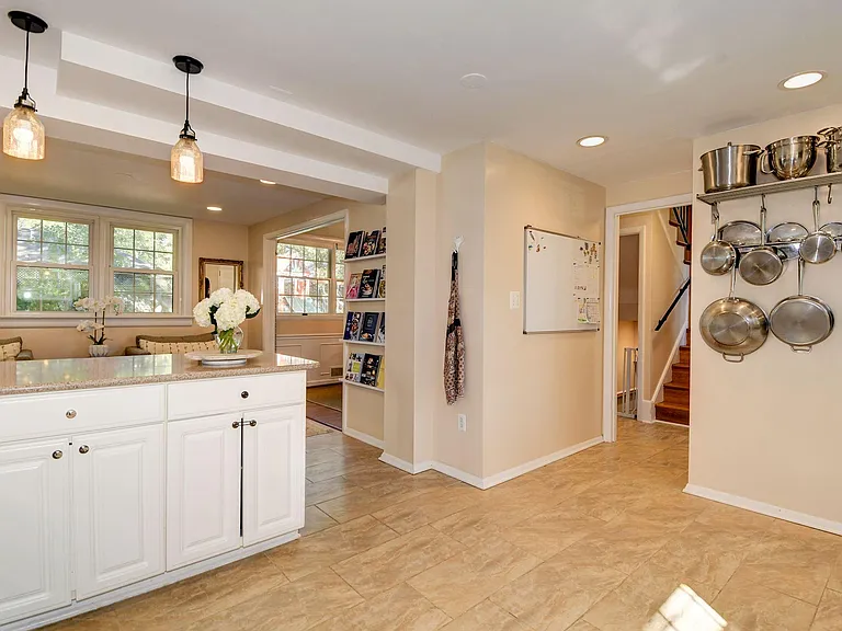 Airy kitchen open to seating area, ready for bar stools at peninsula, with dining room through large opening on the right. Pot rack and bookshelves included. White board not included.