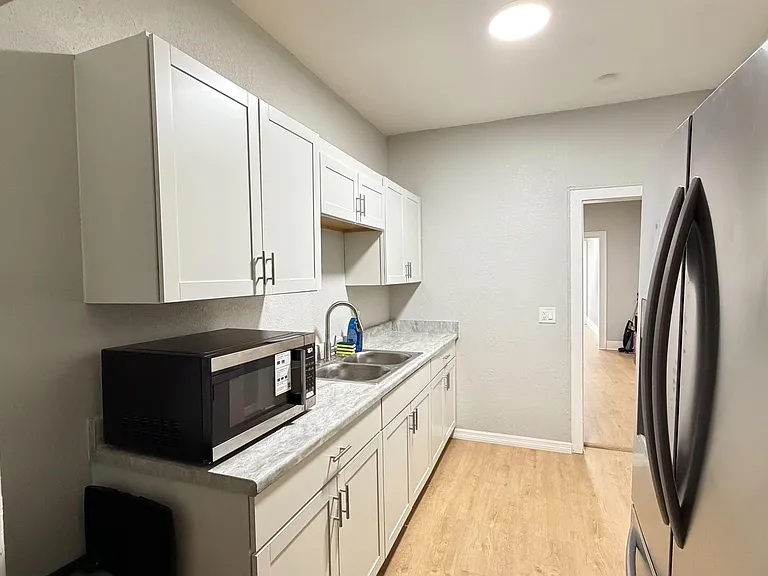 Streamlined galley kitchen with shaker cabinets, ample counter space, double-basin sink, and stainless refrigerator.
