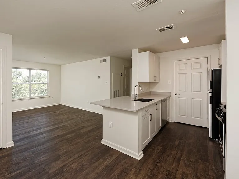 Renovated Package II kitchen and living areas with light grey quartz countertops, white cabinetry, stainless steel appliances, and hard surface flooring
