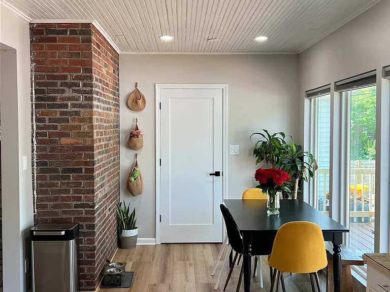 Newly remodeled dining room with floor to ceiling windows, lots of natural light, exposed brick, and an original farmhouse-style ceiling.