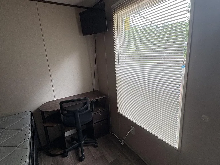 Private bedroom with a large window, wood-look flooring, and a built-in desk area plus wall-mounted TV for studying or stream
