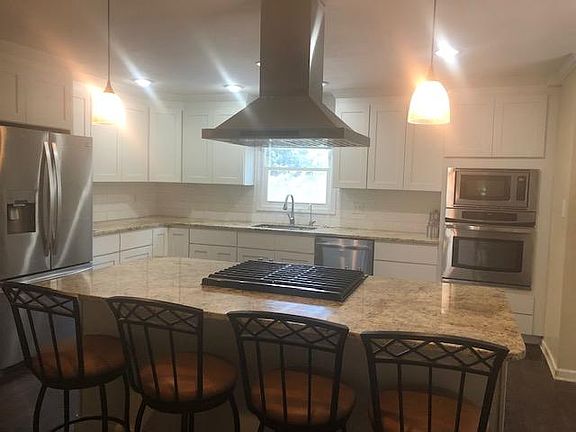 Large open kitchen with island, white shaker cabinets, gas stove top and range, and electric micro/oven combo.