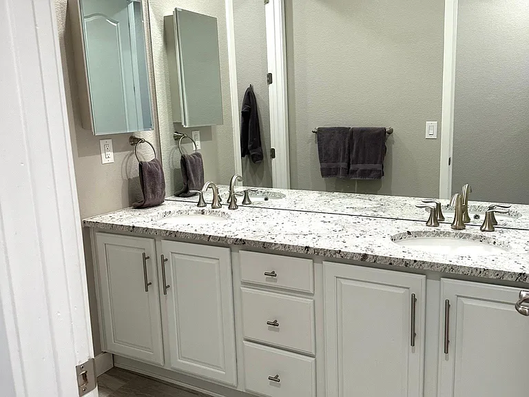 The spacious bathroom includes dual sinks, granite countertops, and attractive tile flooring. Ample cabinet and storage space helps keep everything organized and easily accessible.