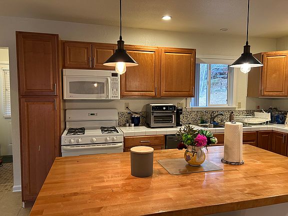 This inviting kitchen features warm wood cabinetry, a spacious butcher block island, and modern appliances. Pendant lighting adds charm, while a large window brings in natural light and offers scenic outdoor views. Perfect for cooking and entertaining!