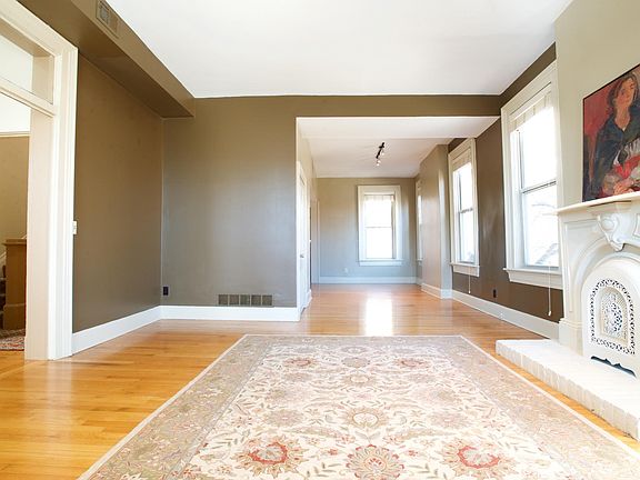 Spacious living room with decorative fireplace and high ceilings and hardwood floors; open floor plan to dining room and kitchen. Many windows for a sunny ambience; all windows have wood blinds.