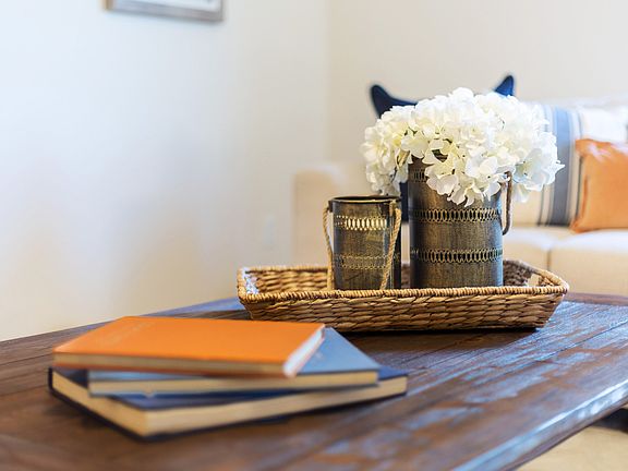 Staged model home with books, woven tray, and white flowers in a coffee can on a wooden table