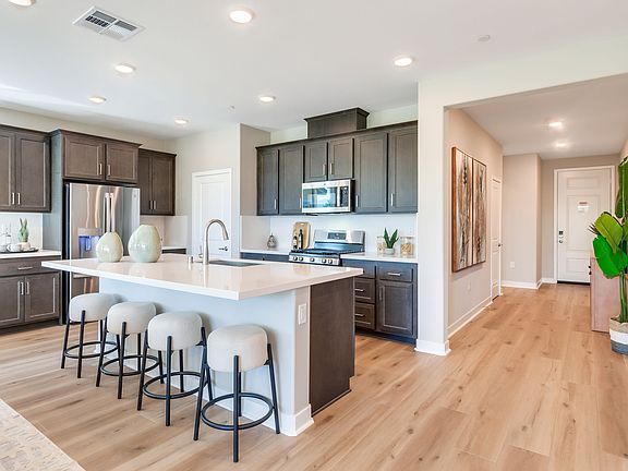 A modern and spacious kitchen with dark wood cabinets, white countertops, and bar stools, leading in