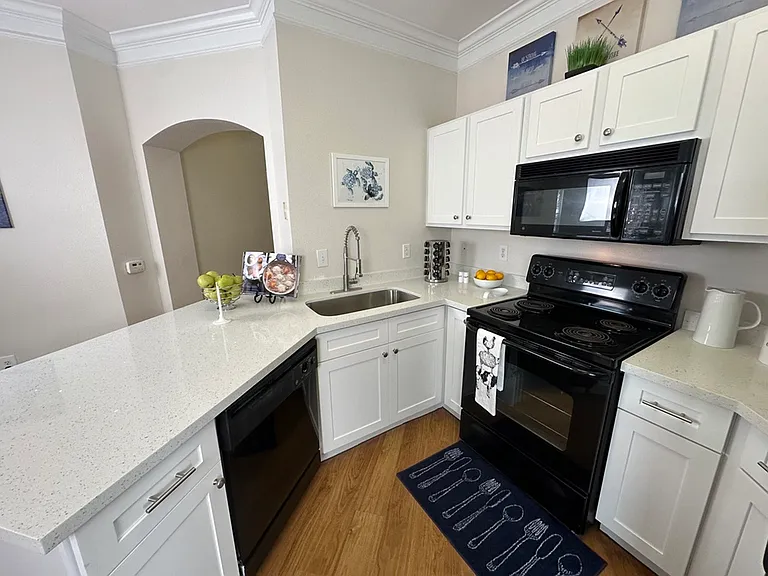 Modern kitchen with sleek black appliances, white cabinetry, and elegant quartz countertop, featuring decorative accents and cozy composite wood flooring. Modern kitchen with sleek black appliances, white cabinetry, and elegant quartz countertop, featurin