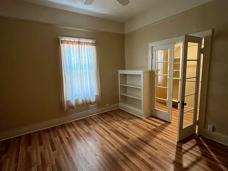 Bedroom with walk-in closet with french doors, built-in bookcase, large window and ceiling fan.