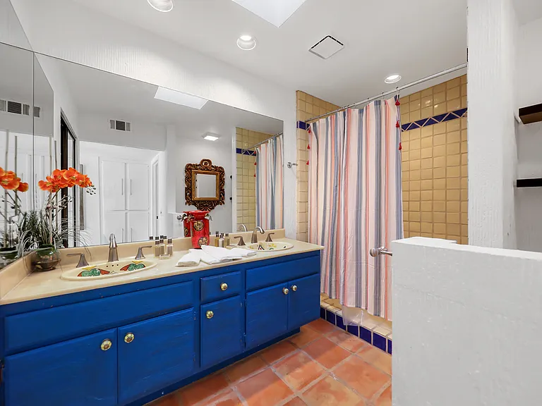 Light-filled bathroom featuring a custom blue double vanity, skylight, and Saltillo tile floors. Spacious, bright, and designed for comfort during longer stays.