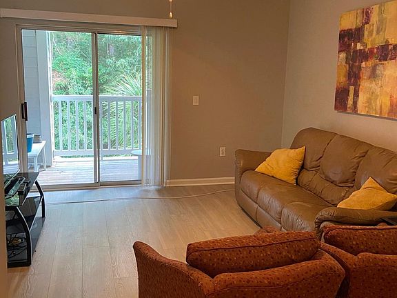 View of living room leading out to balcony which overlooks onto greenery. Television included. Ceiling fan in addition to air conditioning.
