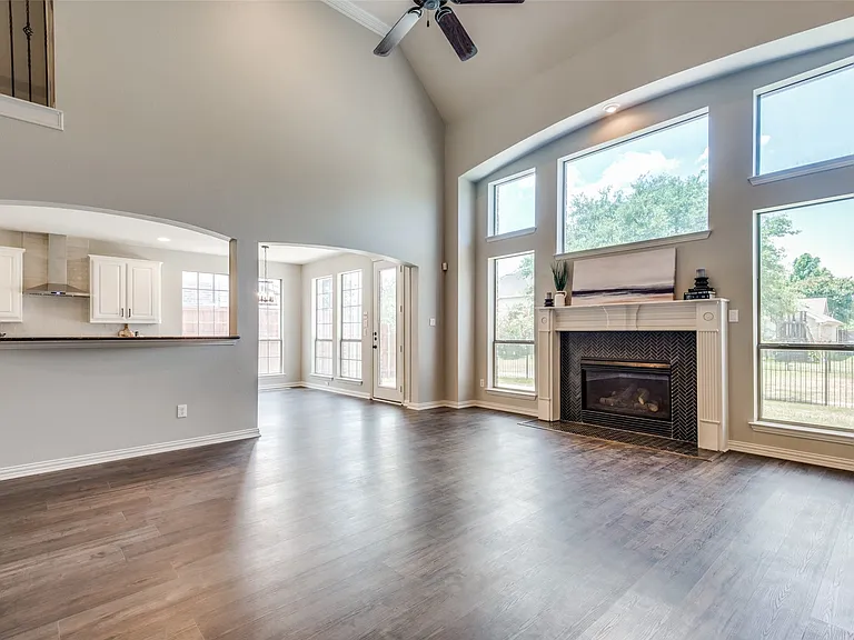 Open-concept living area featuring high vaulted ceilings, wood-finish flooring, and a fireplace with a decorative mantel and dark tile surround