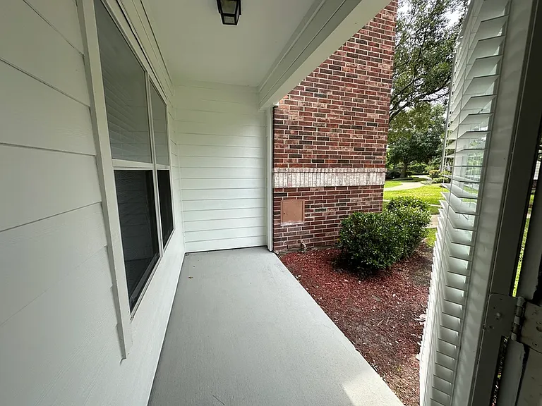 Charming covered porch with white siding and brick accents, overlooking a lush green garden. Charming covered porch with white siding and brick accents, overlooking a lush green garden.