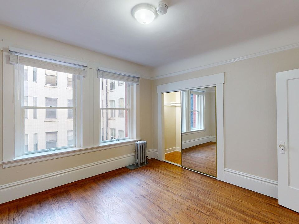 Bright room with wooden floors, large windows, radiator, mirrored closet, ceiling light