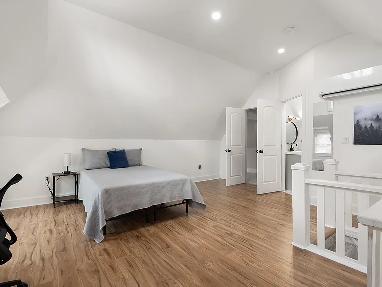 Spacious upstairs bedroom with hardwood-style floors, vaulted ceiling, and convenient access to a nearby sink area.