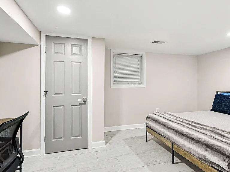 Clean, well-lit bedroom with a comfortable bed, desk workspace, and a window with blinds for privacy and natural light.