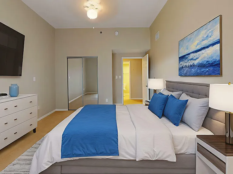 Elegant bedroom with a cozy bed featuring blue accents, modern art, and stylish lighting, creating a serene and inviting atmosphere.