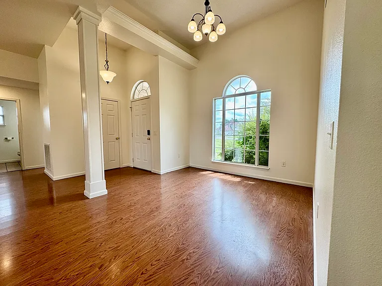 Grand entry with decorative columns, chandelier, hardwood floors, and arched transom windows