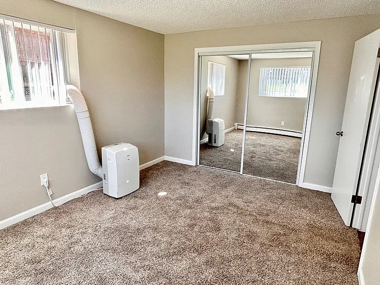 Bright bedroom with plush carpet, mirrored closet doors, and modern portable air conditioner for comfort and style.