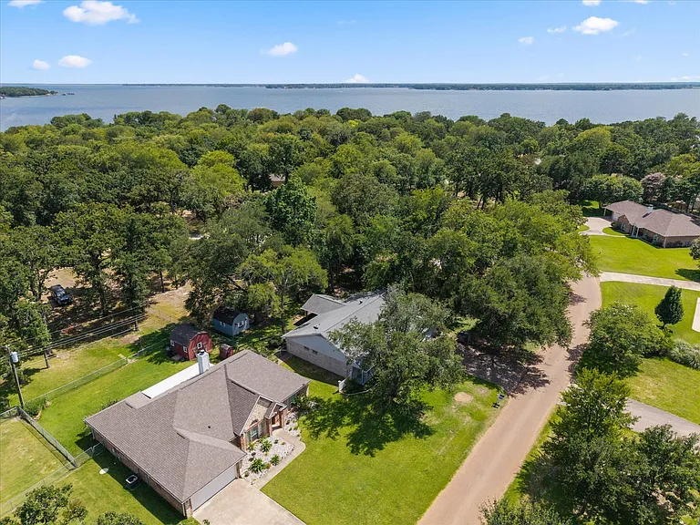 Aerial perspective showcasing a property surrounded by mature trees, with a large body of water visible in the distance