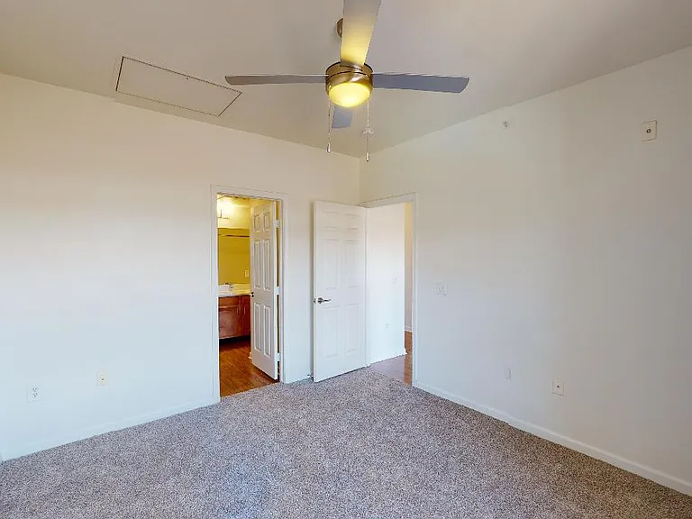 Spacious apartment bedroom with attached bathroom and plush carpet flooring.