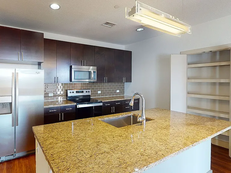Apartment kitchen with stainless steel appliances, granite countertops and wood-style flooring.