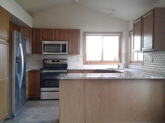 Bright and cherry open concept kitchen with stainless steal appliances, granite and stone backsplash.