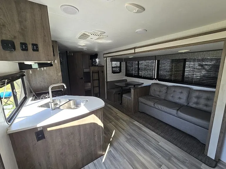 Open-concept living area with sofa seating, dinette nook, and a compact kitchen island with sink and counter space.