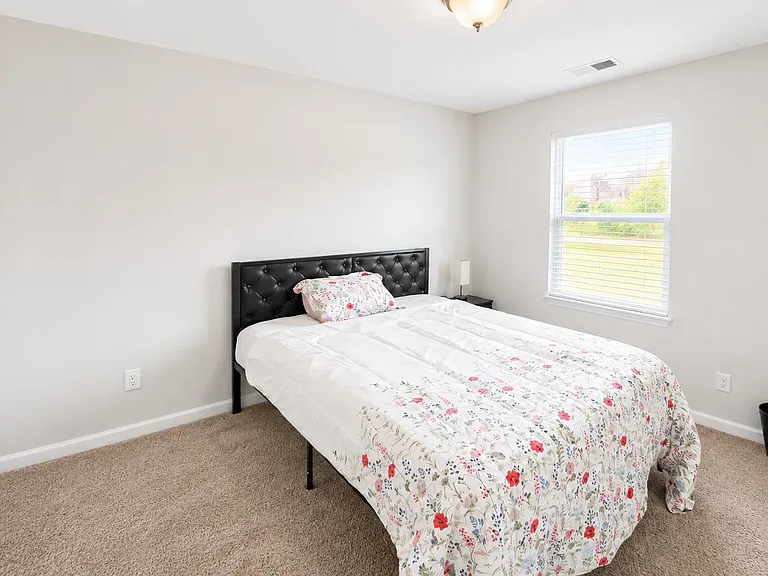 Well-sized bedroom with carpet flooring, a large window with blinds, and space for a nightstand or small desk.