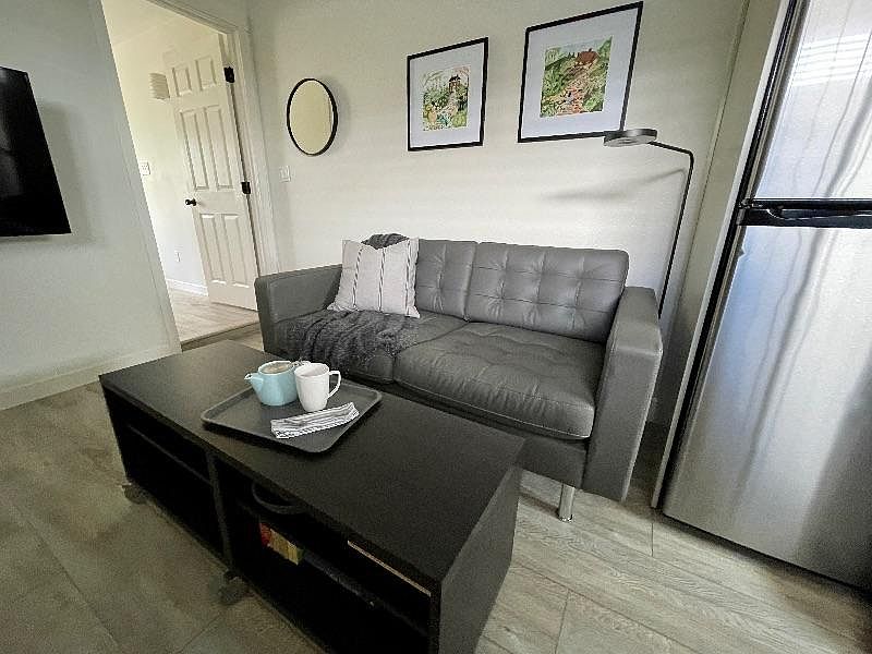 The lounge area features a comfy leather loveseat, coffee table on wheels, reading/task light, and going out mirror. GE refrigerator is whisper silent. Notice the bedroom door to the left and adjustable, wall-mounted FireTV.