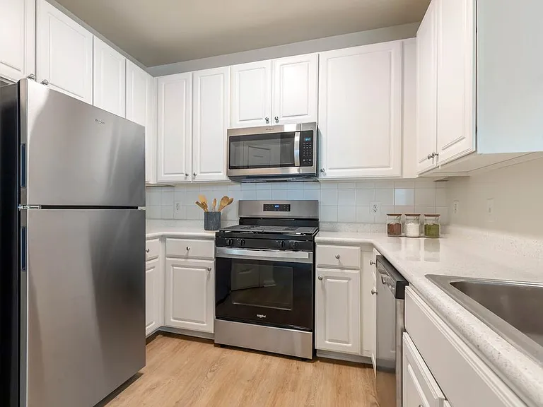 Classic I kitchen with white cabinetry, white laminate countertops, white tile backsplash, stainless steel appliances, and hard surface flooring