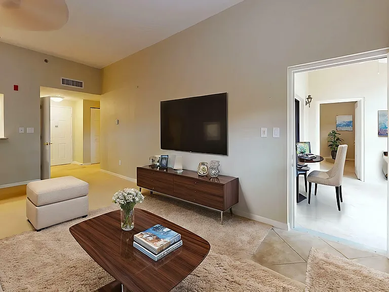 Bright and inviting living room featuring a cozy beige sofa, stylish wooden media console, and an open doorway leading to a chic home office space.