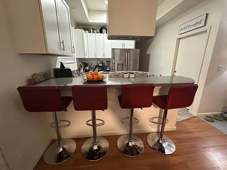 Open kitchen with a long breakfast bar, ample white cabinetry, and stainless-steel refrigerator for easy meal prep.
