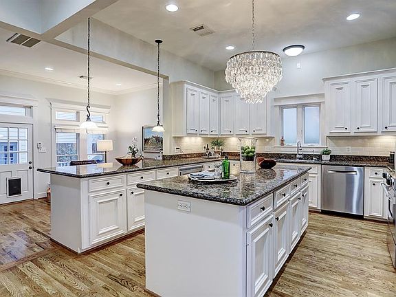 This elegant kitchen has white custom cabinetry, abundant granite counters, stylish stainless appliances, a breakfast bar, an island providing extra storage, and a gorgeous crystal chandelier.