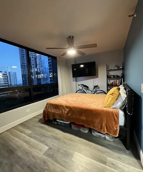 large bedroom with queen bed, smart tv, smart fan, book shelf, beautiful city views