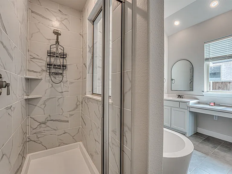 Spacious shower with large format white and gray veined tile, built-in shelving, and a frameless glass enclosure