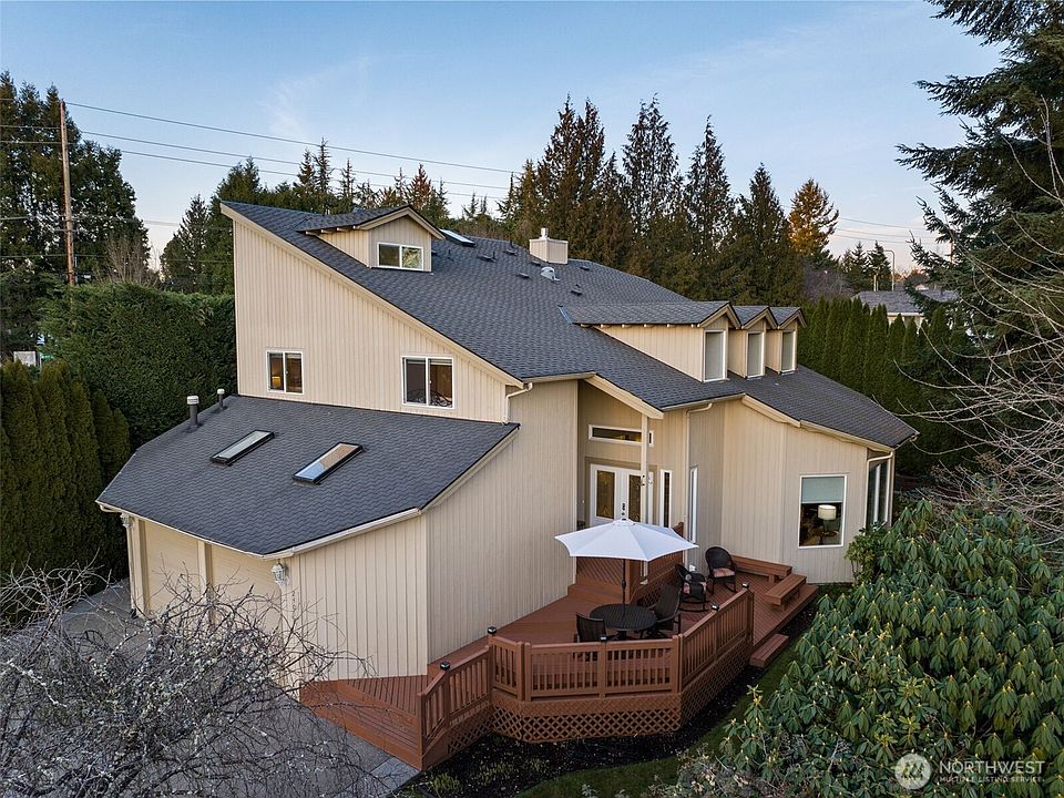 Exterior view of the expansive home featuring a spacious multi-level welcoming deck, mature landscaping, and a peaceful wooded backdrop.>