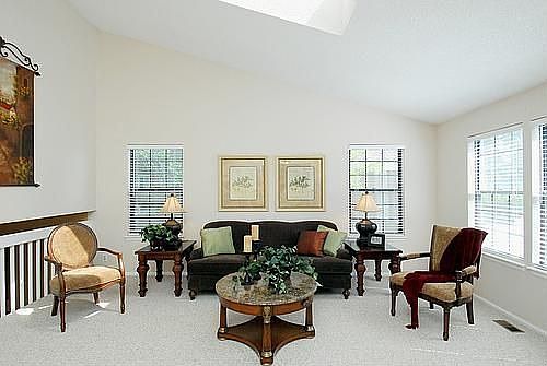 The spacious living room features neutral décor, vaulted ceilings & skylights.