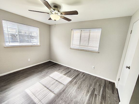 Bright and airy room with elegant dark wood flooring and modern ceiling fan, perfect for a cozy bedroom setup.