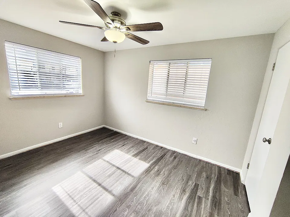 Bright and airy room with elegant dark wood flooring and modern ceiling fan, perfect for a cozy bedroom setup.