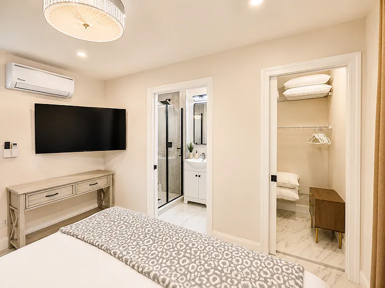 Spacious guest suite sleeping area with private bathroom access, closet storage, smart TV, and modern finishes for added privacy during family or group stays.