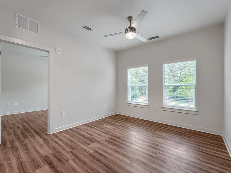 Bedroom with windows and ceiling fan and door leading to living room